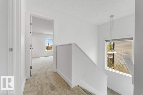 Carpeted hallway and staircase featuring light neutral walls and modern pendant lighting - 7403 Singer Landing Landing, Edmonton, AB - Indoor Photo Showing Other Room