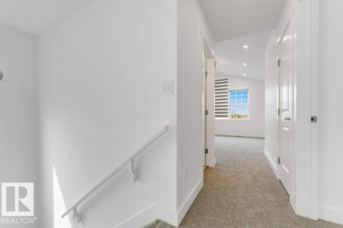 Carpeted hallway with white walls and a white handrail, featuring recessed lighting and a window with horizontal blinds - 7403 Singer Landing Landing, Edmonton, AB - Indoor Photo Showing Other Room
