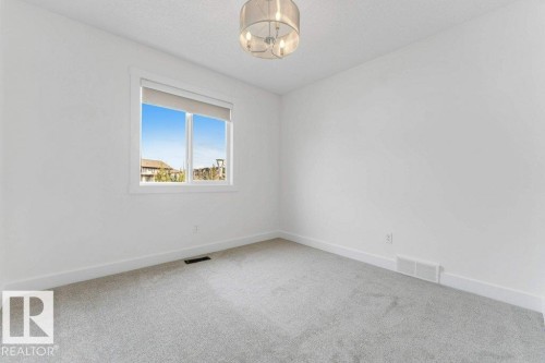 Bright room featuring light gray carpeting, white walls, and a modern drum pendant light fixture - 7403 Singer Landing Landing, Edmonton, AB - Indoor Photo Showing Other Room