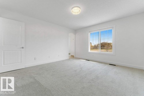 Expansive room featuring light gray carpet flooring, white walls, and a large window with grid panes - 7403 Singer Landing Landing, Edmonton, AB - Indoor Photo Showing Other Room