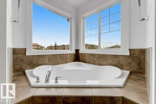 Corner soaking tub with polished chrome fixtures, surrounded by earth-toned tilework and two large windows - 7403 Singer Landing Landing, Edmonton, AB - Indoor Photo Showing Bathroom