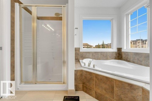 Soaking tub with chrome fixtures, surrounded by brown tile, positioned under multiple windows - 7403 Singer Landing Landing, Edmonton, AB - Indoor Photo Showing Bathroom