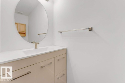 Bathroom vanity with a white countertop and integrated sink, brushed nickel faucet, and a large oval mirror - 7403 Singer Landing Landing, Edmonton, AB - Indoor