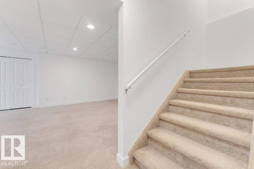 Carpeted staircase with white handrail leading to a spacious room featuring light-toned carpeting, white walls, recessed ceiling lighting, and bi-fold closet doors - 7403 Singer Landing Landing, Edmonton, AB - Indoor Photo Showing Other Room