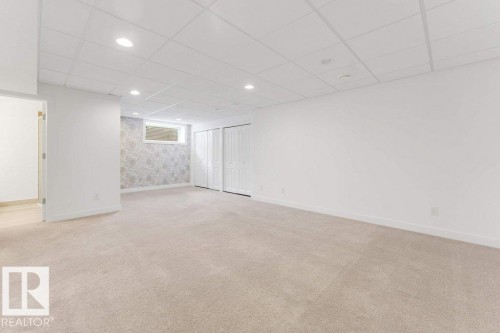 Spacious carpeted room featuring a drop ceiling with recessed lighting, multiple bifold closet doors, a patterned accent wall, and a high-set window - 7403 Singer Landing Landing, Edmonton, AB - Indoor Photo Showing Other Room