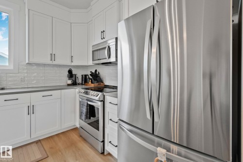 Contemporary kitchen featuring stainless steel appliances, white cabinetry with matte black hardware, light wood-finish flooring, and a subway tile backsplash - 21027 130 Avenue, Edmonton, AB - Indoor Photo Showing Kitchen With Upgraded Kitchen