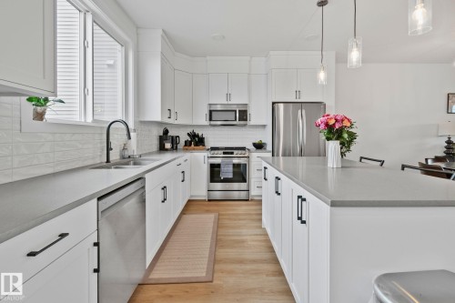 Modern kitchen featuring white cabinetry, stainless steel appliances, a large center island, wood-finish flooring, and a subway tile backsplash - 21027 130 Avenue, Edmonton, AB - Indoor Photo Showing Kitchen With Double Sink With Upgraded Kitchen