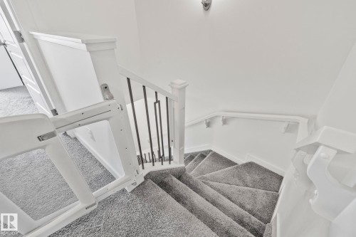 Carpeted staircase featuring a white railing with metal balusters, a wall-mounted handrail, and a built-in safety gate - 21027 130 Avenue, Edmonton, AB - Indoor