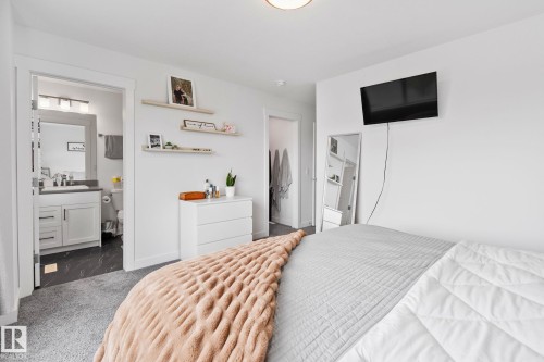 Carpeted room with a doorway opening into a bathroom featuring a white vanity with a gray countertop, a mirror with an overhead light fixture, and dark-toned flooring - 21027 130 Avenue, Edmonton, AB - Indoor Photo Showing Bedroom