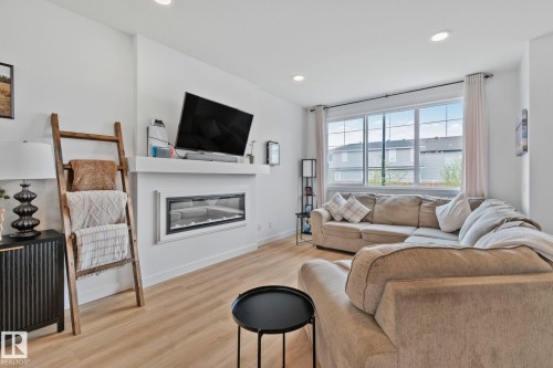 Living area featuring light wood-finish flooring, recessed lighting, a modern linear fireplace with a white mantel, and large multi-pane windows with curtain rods - 21027 130 Avenue, Edmonton, AB - Indoor Photo Showing Living Room With Fireplace