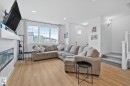 Open-concept living area featuring wood-finish flooring, a contemporary fireplace with a white mantel, and ample natural light from a large window - 21027 130 Avenue, Edmonton, AB  - Indoor Photo Showing Living Room With Fireplace 