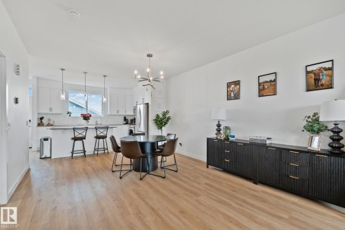 Open-concept kitchen and dining area featuring light wood-finish flooring, white cabinetry, a kitchen island with pendant lighting, and stainless steel appliances - 21027 130 Avenue, Edmonton, AB - Indoor