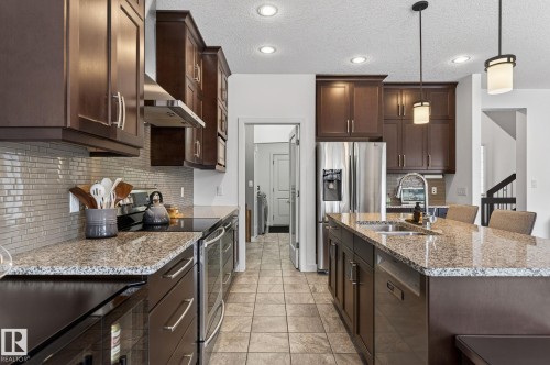 The kitchen features dark wood cabinetry, stainless steel appliances, and granite countertops - 26 Edgewater Terr N, St. Albert, AB - Indoor Photo Showing Kitchen With Double Sink With Upgraded Kitchen