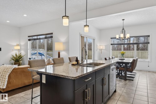 The kitchen features a dark-toned island with a granite countertop, an undermount sink, and pendant lighting - 26 Edgewater Terr N, St. Albert, AB - Indoor Photo Showing Kitchen With Double Sink