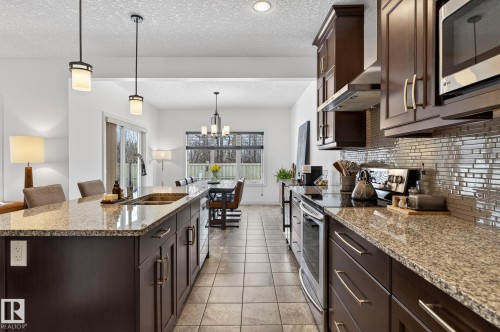 The kitchen features dark wood cabinetry, granite countertops, and stainless steel appliances - 26 Edgewater Terr N, St. Albert, AB - Indoor Photo Showing Kitchen With Double Sink With Upgraded Kitchen