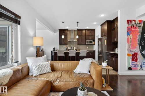 The property features an open living area with hardwood flooring, leading into a kitchen with dark wood cabinetry, stainless steel appliances, and a breakfast bar - 26 Edgewater Terr N, St. Albert, AB - Indoor Photo Showing Living Room