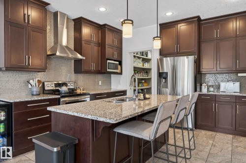The kitchen features extensive dark wood cabinetry, stainless steel appliances including a range and refrigerator, and a large island with a stone countertop and seating - 26 Edgewater Terr N, St. Albert, AB - Indoor Photo Showing Kitchen With Double Sink With Upgraded Kitchen