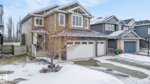 The property features a two-story exterior with textured siding and stone accents, a prominent front entrance with a porch, and an attached two-car garage with white paneled doors - 26 Edgewater Terr N, St. Albert, AB - Outdoor With Facade