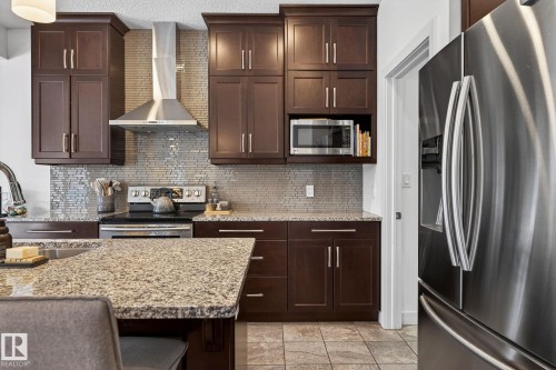 The kitchen features dark wood cabinetry, granite countertops, a stainless steel refrigerator, and a tiled backsplash - 26 Edgewater Terr N, St. Albert, AB - Indoor Photo Showing Kitchen With Upgraded Kitchen