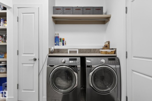 Laundry area featuring a pair of front-loading machines, a countertop with a tiled backsplash, and a floating shelf with a hanging rod - 26 Edgewater Terr N, St. Albert, AB - Indoor Photo Showing Laundry Room