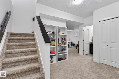 This property features a carpeted staircase with a dark wood handrail, an inviting open entryway with built-in shelving, and a carpeted living area visible in the background - 26 Edgewater Terr N, St. Albert, AB - Indoor Photo Showing Other Room