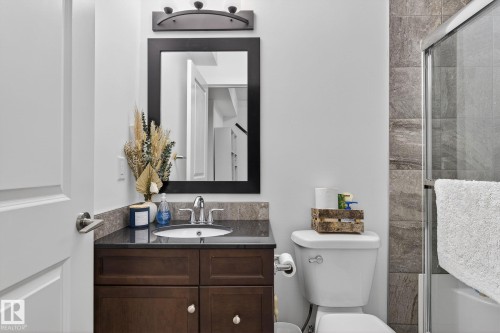 Bathroom featuring a dark wood vanity with a stone countertop, a white sink with a chrome faucet, a rectangular mirror, and a shower with glass doors and tiled walls - 26 Edgewater Terr N, St. Albert, AB - Indoor Photo Showing Bathroom