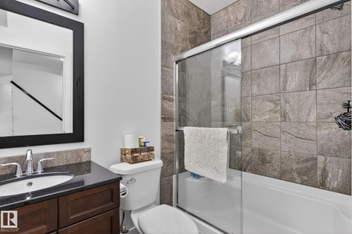 The bathroom features a vanity with a dark countertop and cabinetry, a toilet, and a shower-tub combination with sliding glass doors and tiled walls - 26 Edgewater Terr N, St. Albert, AB - Indoor Photo Showing Bathroom