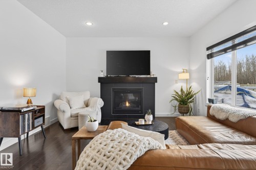 Living area featuring dark hardwood floors, a fireplace with a black tile surround, and large windows offering exterior views - 26 Edgewater Terr N, St. Albert, AB - Indoor Photo Showing Living Room With Fireplace