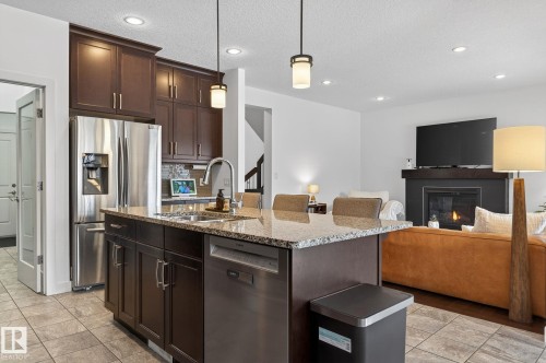 The kitchen features a large island with a granite countertop, a stainless steel refrigerator, and dark wood cabinetry - 26 Edgewater Terr N, St. Albert, AB - Indoor Photo Showing Kitchen With Upgraded Kitchen