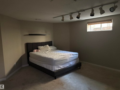 Neutral-toned room featuring a single window with blinds, ceiling-mounted track lighting, and a wall-mounted shelf - 3516 49 Avenue, Drayton Valley, AB - Indoor Photo Showing Bedroom