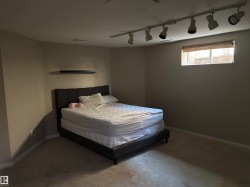Neutral-toned room featuring a single window with blinds, ceiling-mounted track lighting, and a wall-mounted shelf - 