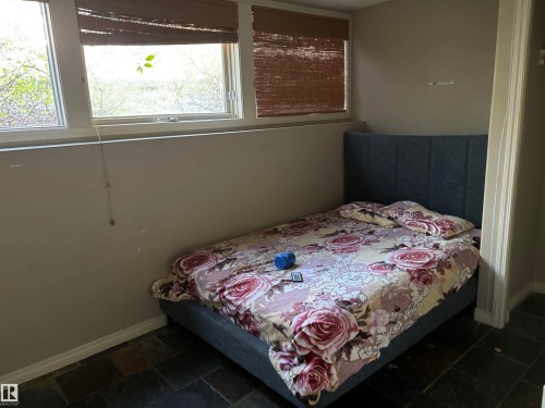 Room featuring multiple windows with natural wood-tone blinds, neutral painted walls, white baseboards, and dark-toned slate-style floor tiling - 3516 49 Avenue, Drayton Valley, AB - Indoor Photo Showing Bedroom