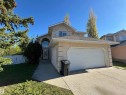 Two-story stucco exterior featuring an arched window above the front entrance, a two-car garage with a panel door, a concrete driveway, and mature landscaping elements - 3516 49 Avenue, Drayton Valley, AB  - Outdoor 