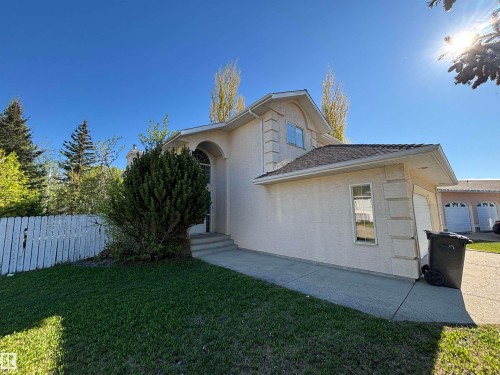 Stucco exterior featuring an arched entryway, shingle roofing, and an attached garage with a single window - 3516 49 Avenue, Drayton Valley, AB - Outdoor