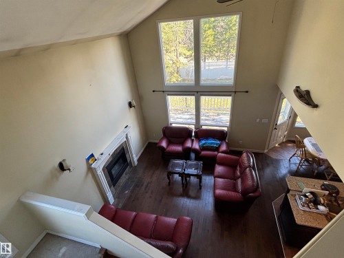 Two-story living area with vaulted ceilings, a fireplace with a white mantel and stone surround, wood-finish flooring, and multiple windows - 3516 49 Avenue, Drayton Valley, AB - Indoor