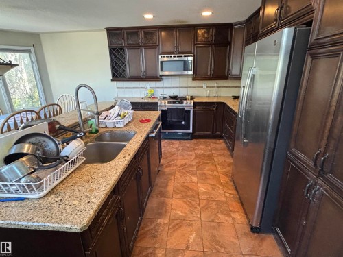 Kitchen featuring dark wood cabinetry, light granite countertops, and a tile backsplash - 3516 49 Avenue, Drayton Valley, AB - Indoor Photo Showing Kitchen With Stainless Steel Kitchen With Double Sink With Upgraded Kitchen