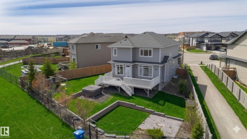 Rear exterior featuring a spacious elevated deck with white railings, a fully fenced yard with a hot tub, and a tiered garden bed - 62 Ellice Bend, Fort Saskatchewan, AB - Outdoor