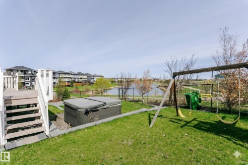 Lawn backyard with a wooden deck featuring white railings and stairs, a covered hot tub, and a wooden swing set - 62 Ellice Bend, Fort Saskatchewan, AB - Outdoor
