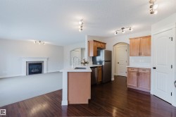 Open-concept kitchen and living area featuring dark wood-finish flooring, a kitchen island with a built-in sink, light wood cabinetry, white countertops, and a living area with a fireplace - 