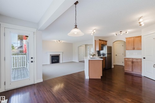 Open-concept design featuring rich wood-finish flooring, a contemporary kitchen with stainless steel appliances, and a living area with a built-in fireplace - 1140 115 Street, Edmonton, AB - Indoor Photo Showing Kitchen With Fireplace