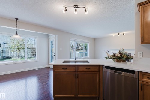 Kitchen featuring wood-finish cabinetry, light-toned countertops, a built-in stainless steel dishwasher, and an undermount sink - 1140 115 Street, Edmonton, AB - Indoor Photo Showing Kitchen With Double Sink