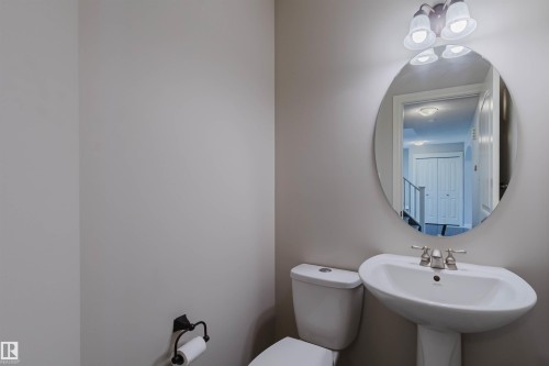 Bathroom featuring an oval mirror, three-light vanity fixture, pedestal sink, and toilet with a wall-mounted toilet paper holder - 1140 115 Street, Edmonton, AB - Indoor Photo Showing Bathroom