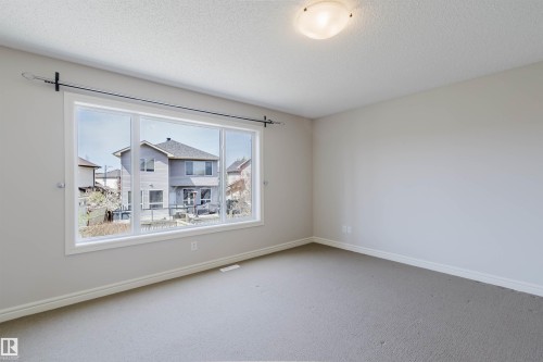 Spacious room featuring a large multi-pane window, neutral-toned walls, gray carpeting, white baseboards, and a semi-flush mount ceiling light fixture - 1140 115 Street, Edmonton, AB - Indoor Photo Showing Other Room