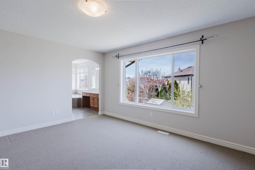 Carpeted room featuring a large window, an arched doorway, and light gray walls - 1140 115 Street, Edmonton, AB - Indoor Photo Showing Other Room