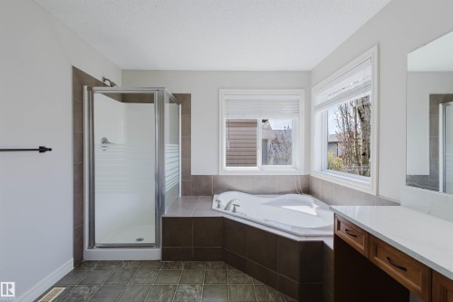 Spacious bathroom featuring an enclosed glass shower, an oversized corner soaking tub, a vanity with a white countertop, wood-finish cabinetry, and tiled flooring - 1140 115 Street, Edmonton, AB - Indoor Photo Showing Bathroom