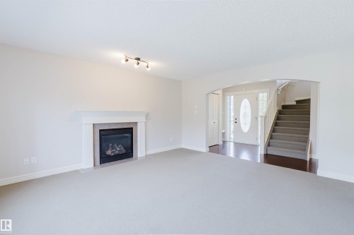 Spacious living area featuring a gas fireplace with a white mantel, light-toned carpeting, and a track lighting fixture - 1140 115 Street, Edmonton, AB - Indoor Photo Showing Living Room With Fireplace
