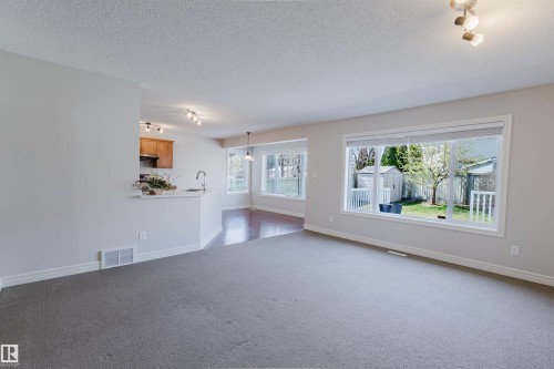 Spacious living area featuring neutral carpeting, a large picture window, and a built-in breakfast bar - 1140 115 Street, Edmonton, AB - Indoor