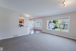 Spacious living area featuring neutral carpeting, a large picture window, and a built-in breakfast bar - 