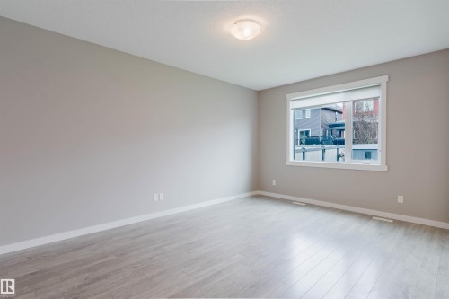 Spacious room featuring light wood-finish flooring, neutral wall tones, a large window with white trim, and a flush-mount ceiling light fixture - 7827 18 Avenue, Edmonton, AB - Indoor Photo Showing Other Room