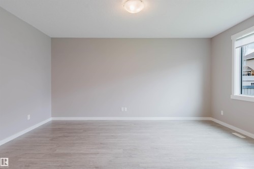 Spacious room featuring light wood-finish flooring, neutral wall paint, white baseboards, and a large window with white trim - 7827 18 Avenue, Edmonton, AB - Indoor Photo Showing Other Room